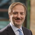 Carlo Matildi, Managing Director, outside in front of a blurred brown background featuring a building and mix of natural and urban elements.