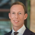 Portrait of Dennis de Wolf, Director, Real Estate, outside in front of a blurred brown background featuring a building and mix of natural and urban elements.