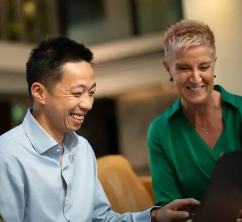 Three colleague gathered around a laptop laughing and engaging in conversation.