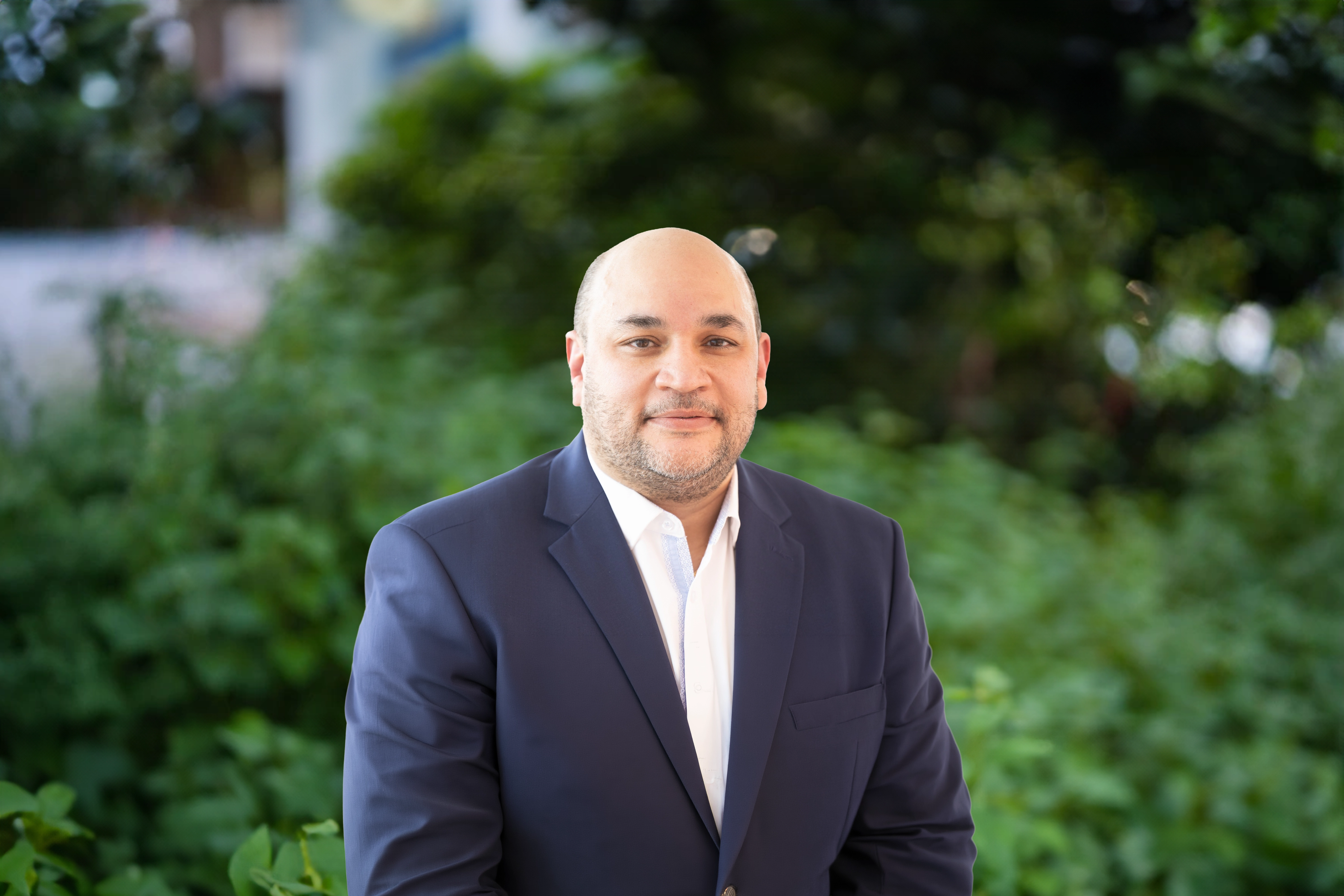 Jawad Masud, standing outside next to green bushes, smiling.