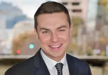 Portrait of Colin McBride, Director of Real Estate, Hong Kong and Macau, Standing outside featuring an urban cityscape with tall buildings and a mix of architectural styles. The scene includes some trees with autumn foliage, adding a touch of color. 