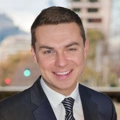 Portrait of Colin McBride, Director of Real Estate, Hong Kong and Macau, Standing outside featuring an urban cityscape with tall buildings and a mix of architectural styles. The scene includes some trees with autumn foliage, adding a touch of color.