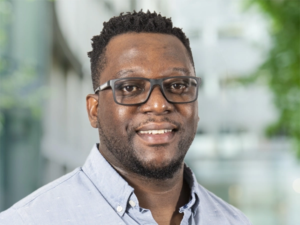 Gerald Madondo, Country Director, standing outside in front of an outdoor urban setting, featuring modern architectural elements with clean lines. There are hints of greenery, suggesting some trees or plants.