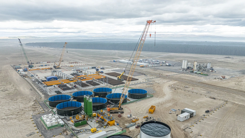 Aerial view of port buildings and storage facilities under construction in the foreground, looking out towards the sea in the distance