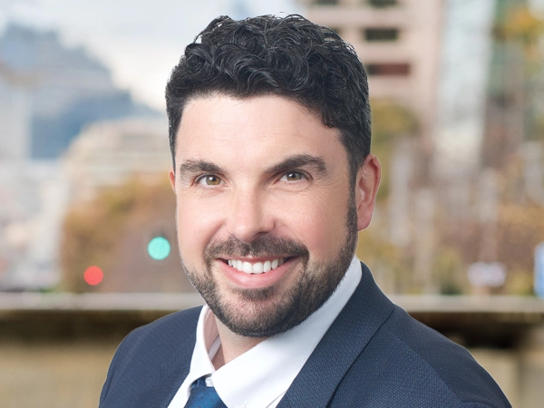Michael Hardman, Vice President,  standing outside featuring an urban cityscape with tall buildings and a mix of architectural styles. The scene includes some trees with autumn foliage, adding a touch of color. 