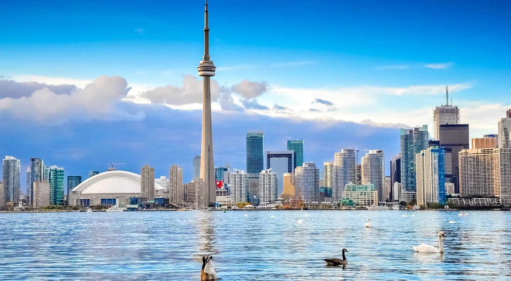 Toronto skyline viewed from across lake Ontario, featuring the CN tower prominently in the centre, with the Rogers centre dome visible to the left.