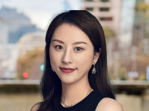 Kexin Sun outside in front of a blurred brown background featuring a building and mix of natural and urban elements.