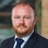 David Griffiths, Director, Real Estate Lead, UAE, outside in front of a blurred brown background featuring a building and mix of natural and urban elements.