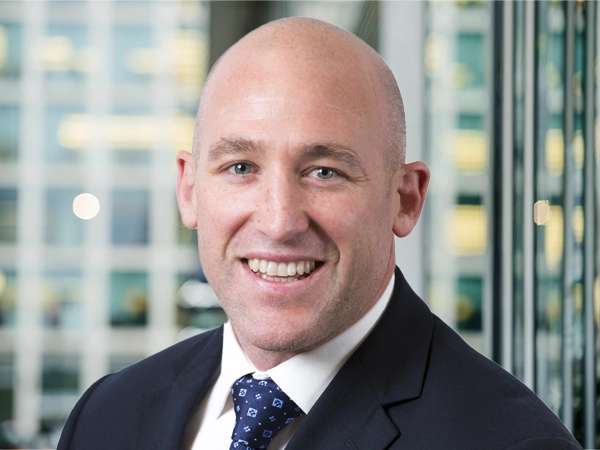 Portrait of Simon Kearney, Director - Real estate, with city landscape featuring building with lots of windows in the background.