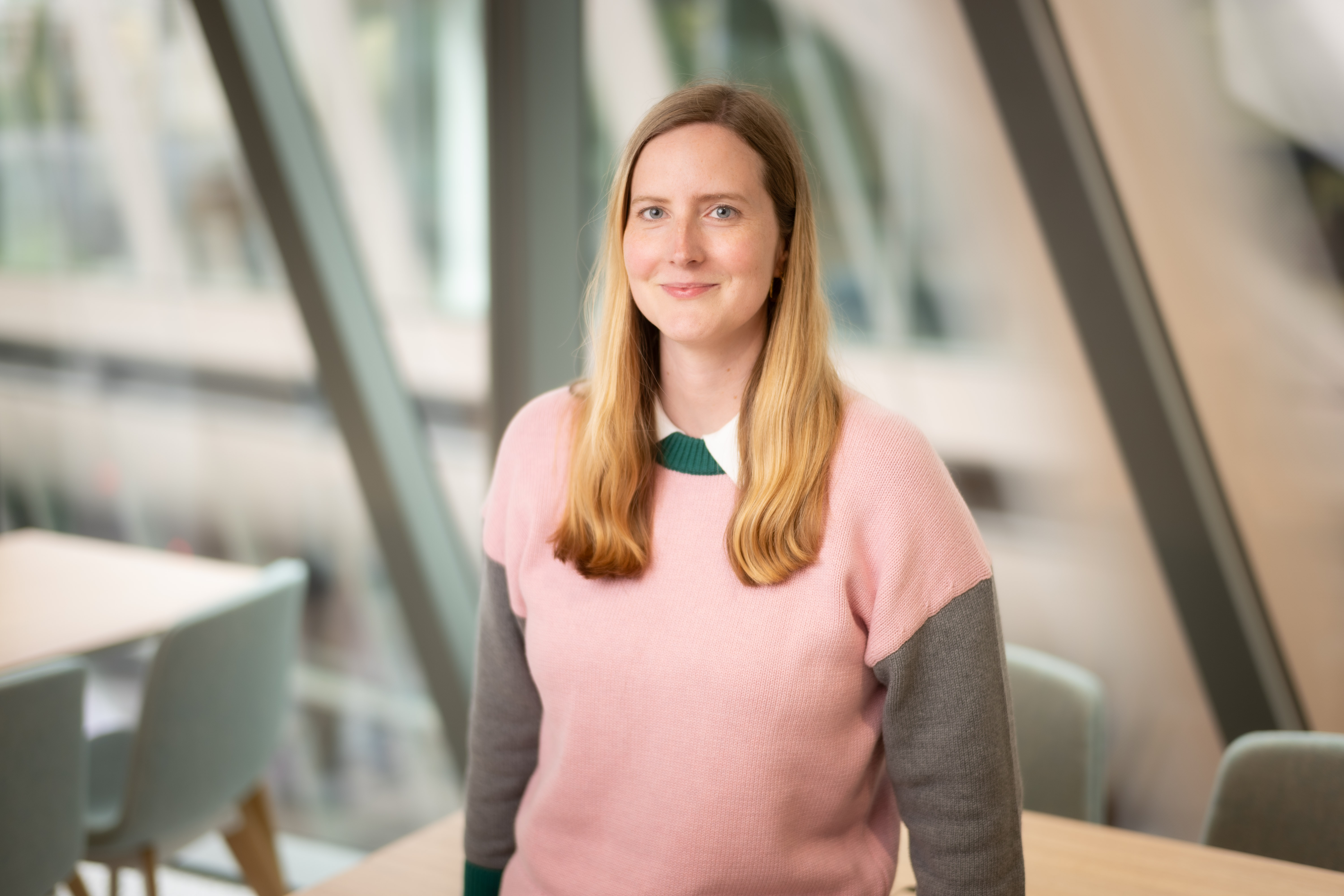 Portrait of Marissa Stenning inside office standing infront of windows in pink jumper