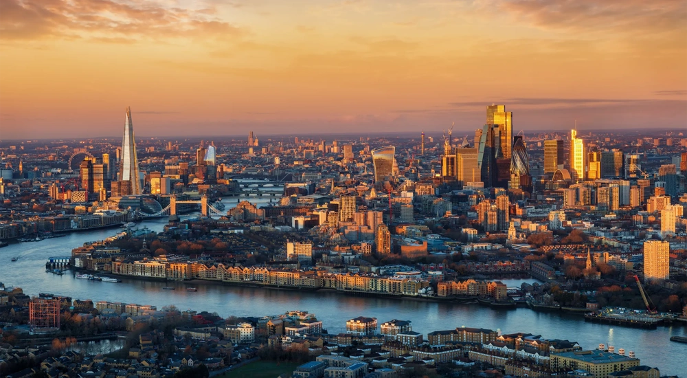 Panoramic, elevated view of the urban London skyline with soft, golden sunlight during sunrise, England