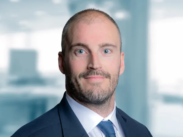 Portrait of Dean Furey Director, Middle East/KSA, standing in blue suit in blurred office background