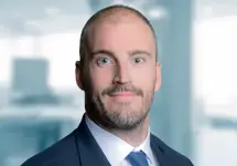 Portrait of Dean Furey Director, Middle East/KSA, standing in blue suit in blurred office background