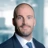 Portrait of Dean Furey Director, Middle East/KSA, standing in blue suit in blurred office background