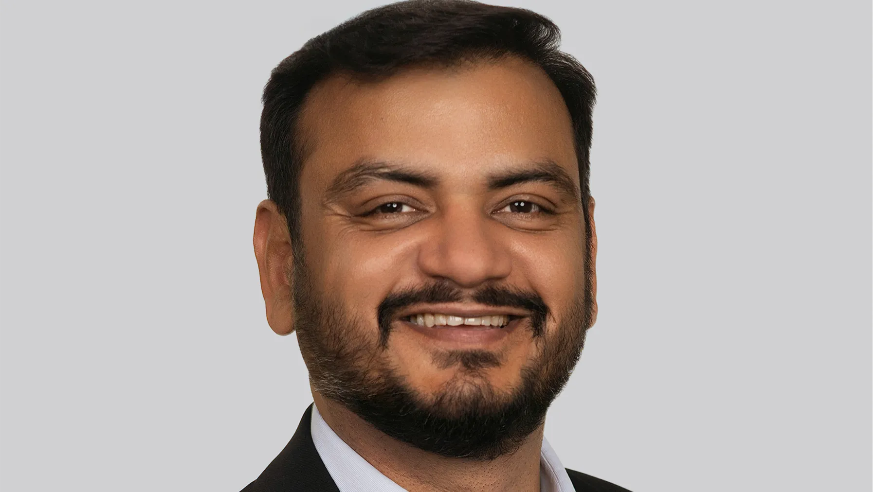 Portrait of Ashish Jain, Managing Directer, Canada, smiling against grey background.