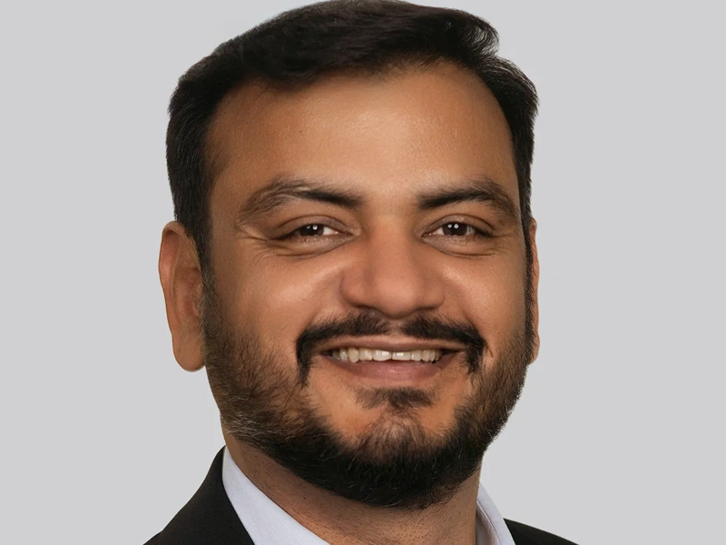 Portrait of Ashish Jain, Managing Directer, Canada, smiling against grey background.