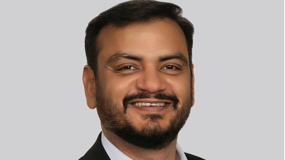 Portrait of Ashish Jain, Managing Directer, Canada, smiling against grey background.