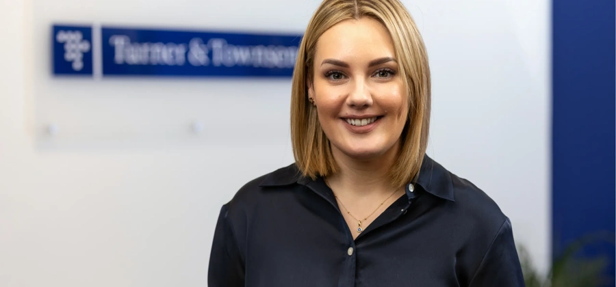 Portrait of Steph Marahall, Managing Director, UK Cost Management, standing in office in front of Turner & Townsend sign