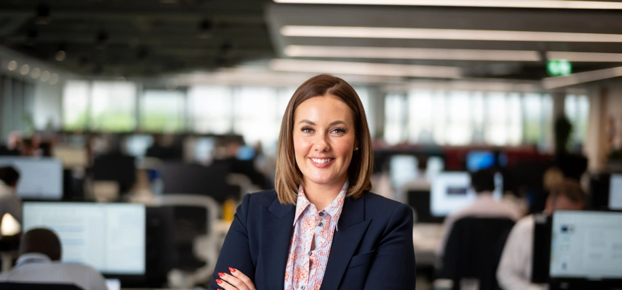 Portrait of Steph Marahall, Managing Director, UK Cost Management, standing in office in front of Turner & Townsend sign