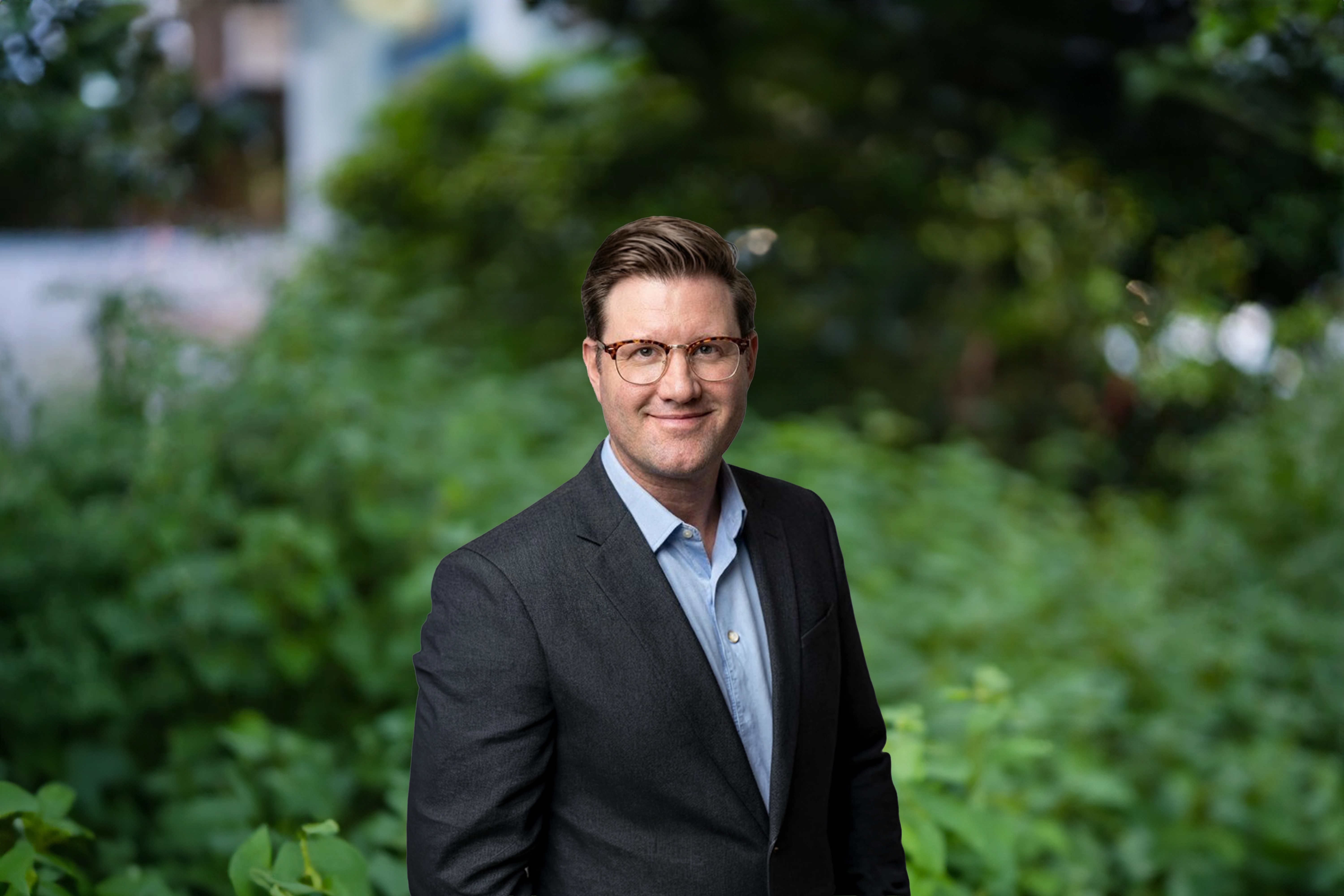 Sean Halpin, standing outside next to green bushes, smiling.