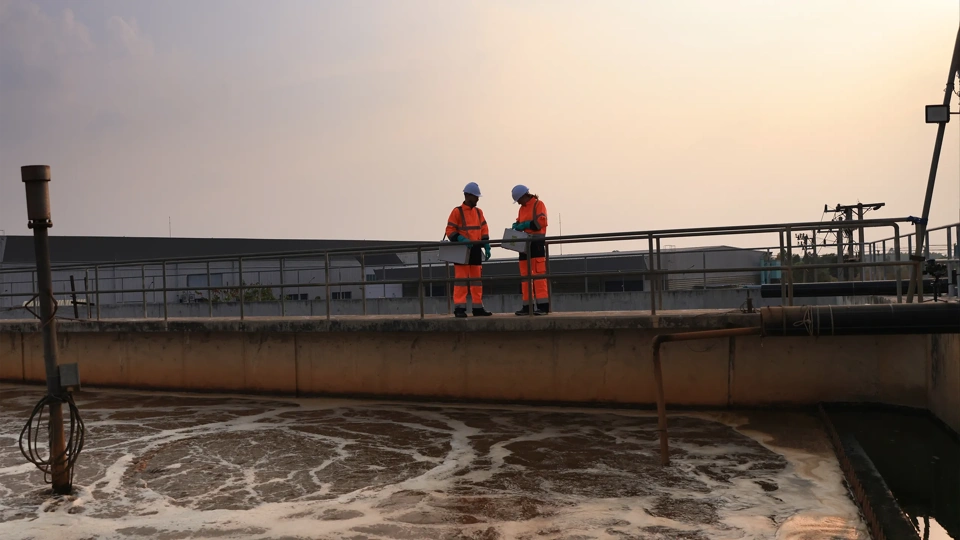 Safety and environmental engineers Working on the sunlight at a wastewater treatment plant in the industrial estate by walking around and checking the quality of the water