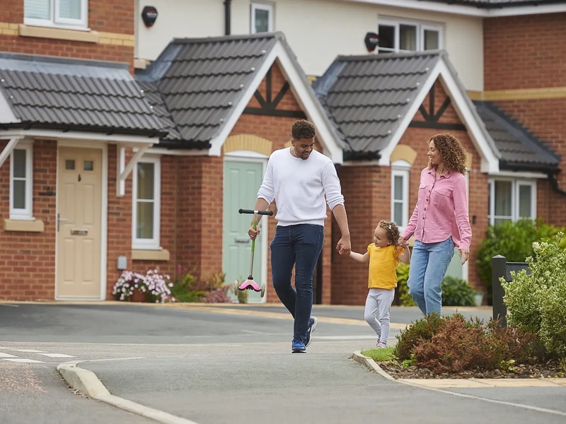 Two adults holding the hand of a child in yellow top outside of housing estate