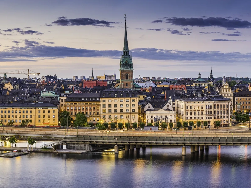 High angle panoramic view across the rooftops and spires of Gamla Stan as the dusk lights illuminate the heart of Stockholm, Sweden's vibrant capital city.