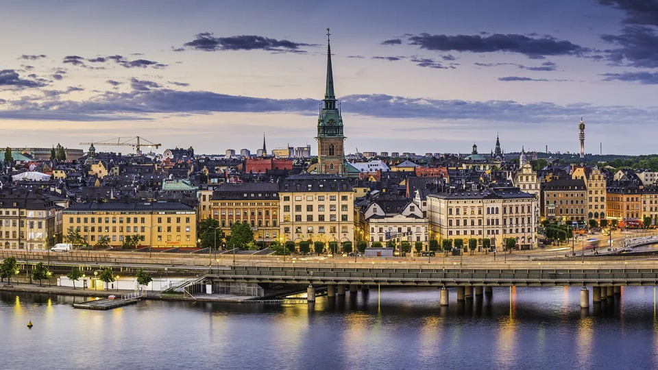 High angle panoramic view across the rooftops and spires of Gamla Stan as the dusk lights illuminate the heart of Stockholm, Sweden's vibrant capital city.
