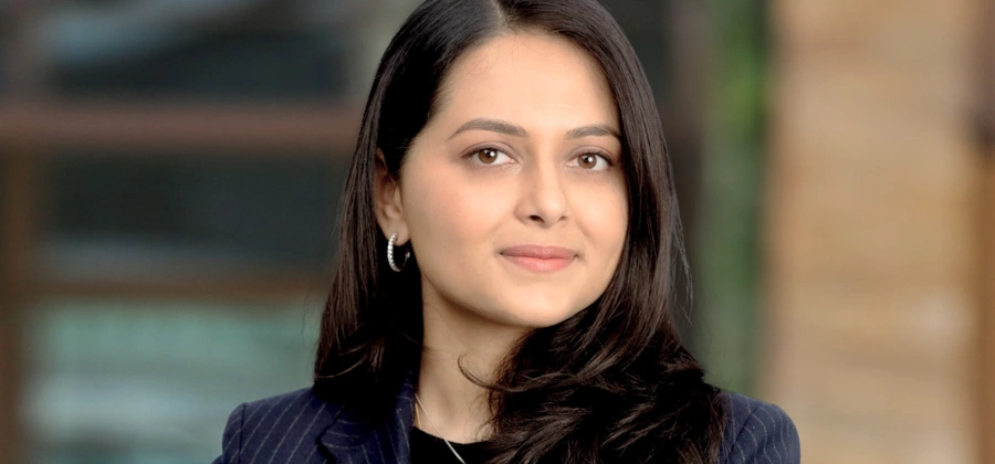 Portrait of Aparna Servansingh, Associate Director, outside in front of a blurred brown background featuring a building and mix of natural and urban elements.