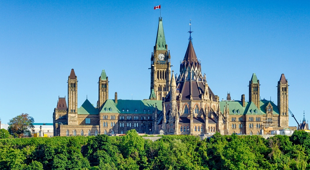 Parliament building in Ottawa, Canada with clock tower flying Canadian flag against a blue sky