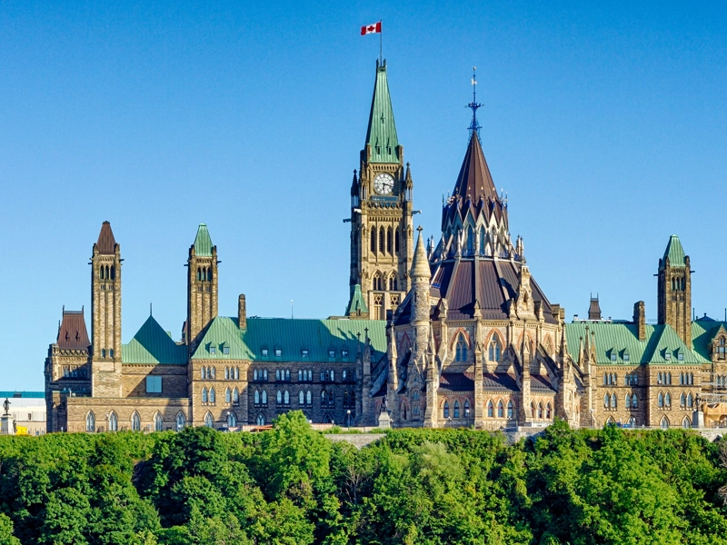 Parliament building in Ottawa, Canada with clock tower flying Canadian flag against a blue sky