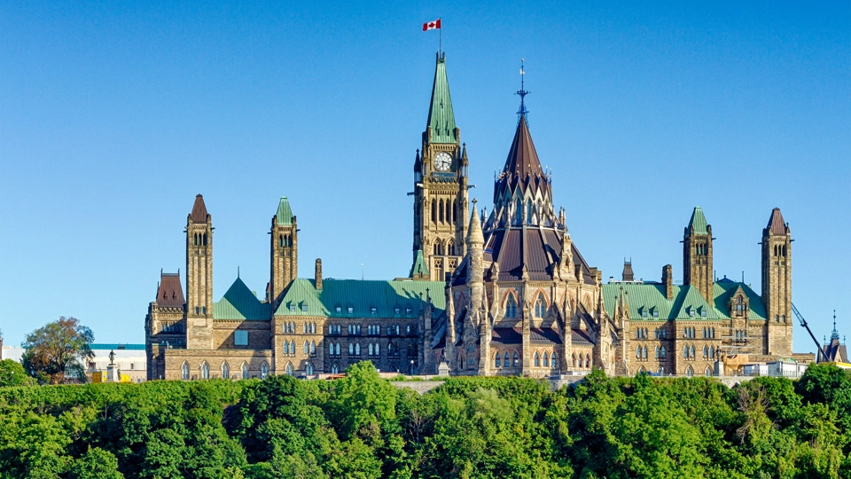 Parliament building in Ottawa, Canada with clock tower flying Canadian flag against a blue sky