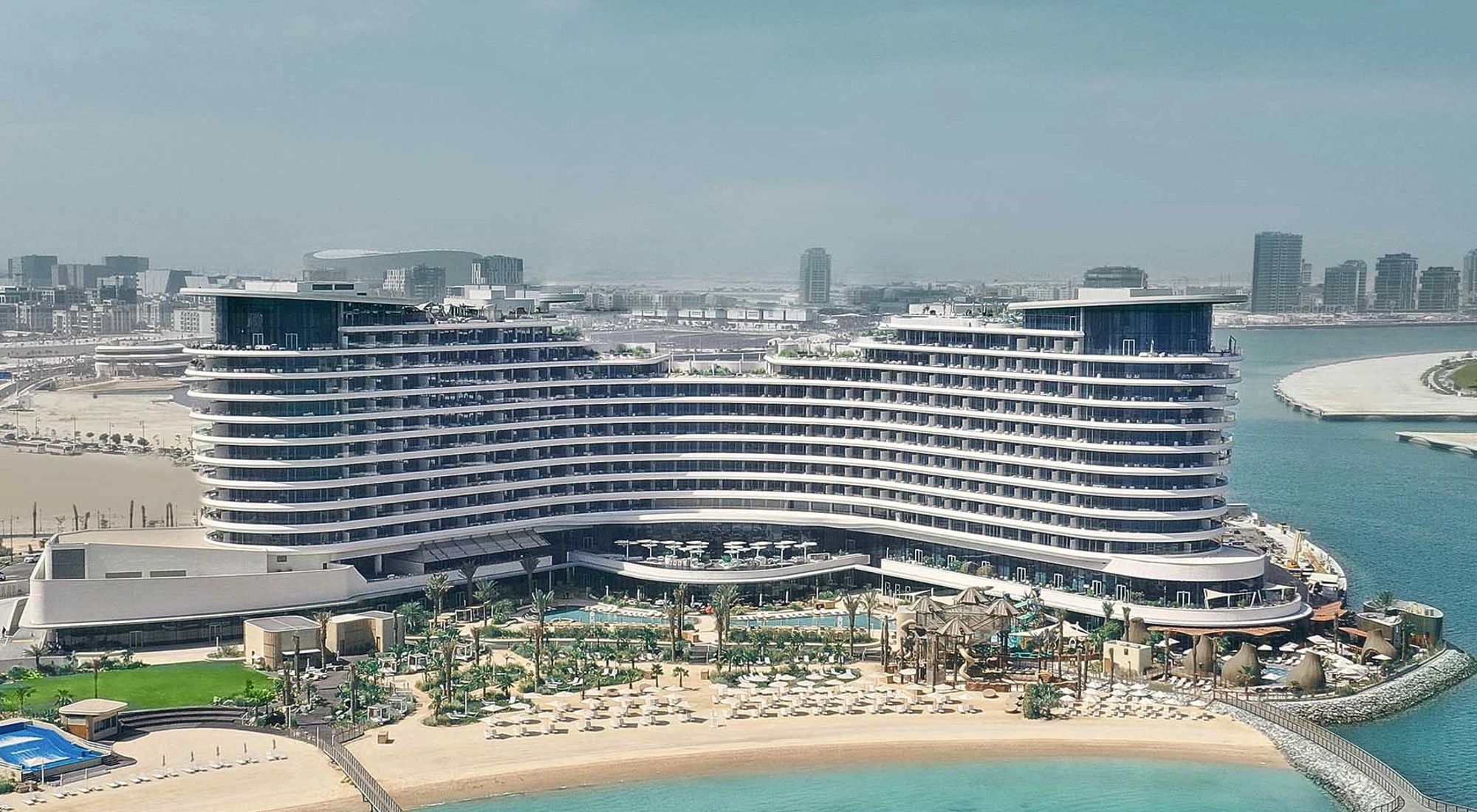 A beach front multi-story hotel resort complex with sun loungers and the sea in the foreground.