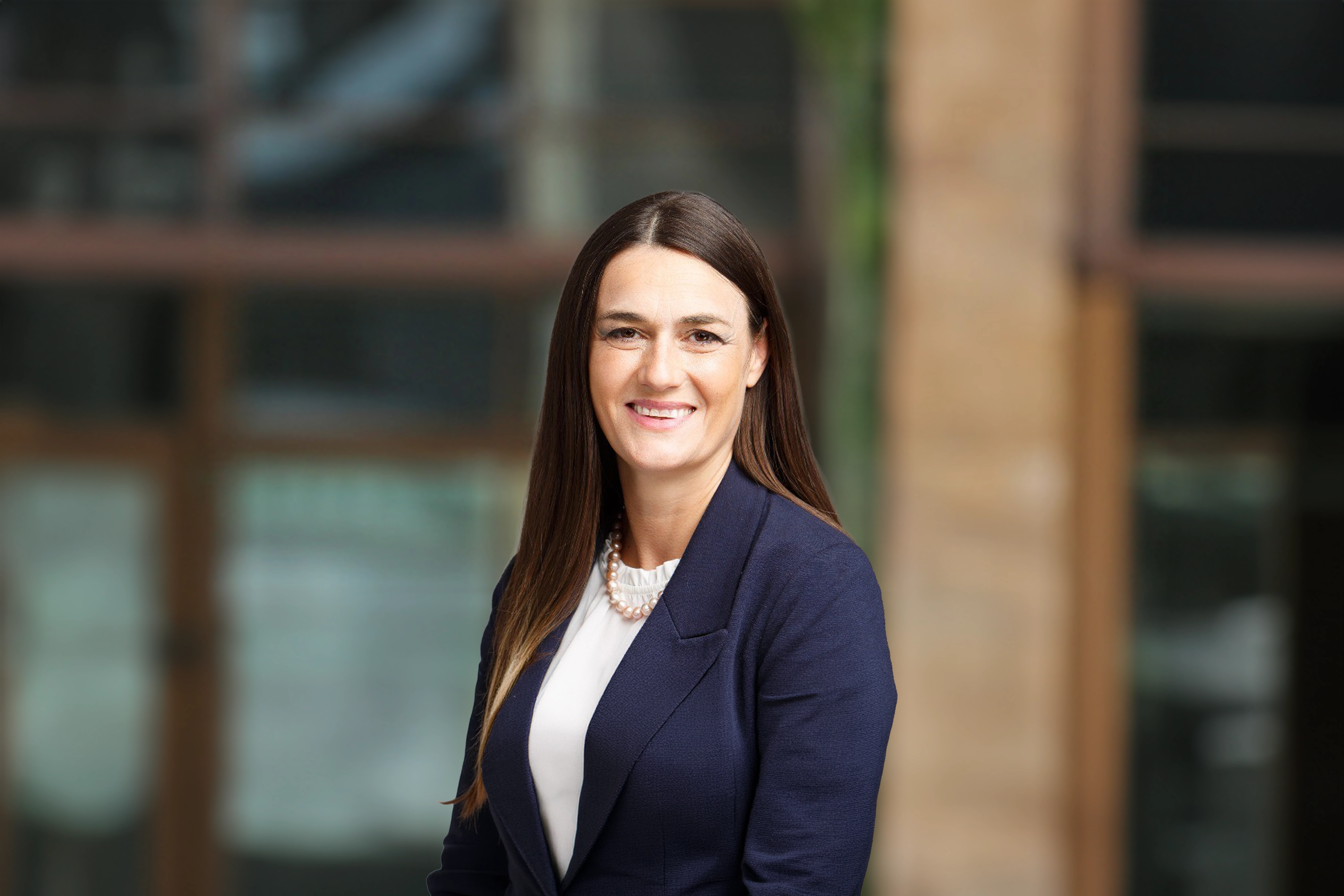 Anna Rosa, Clean energy sector lead, outside in front of a blurred brown background featuring a building and mix of natural and urban elements.