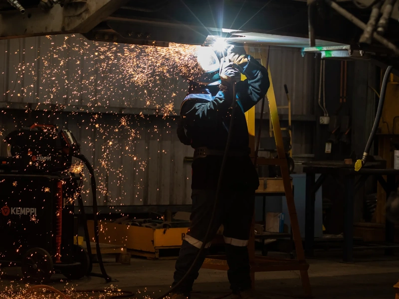 Welder in protective equipment works on a raised project in a dimly lit workshop, Australia