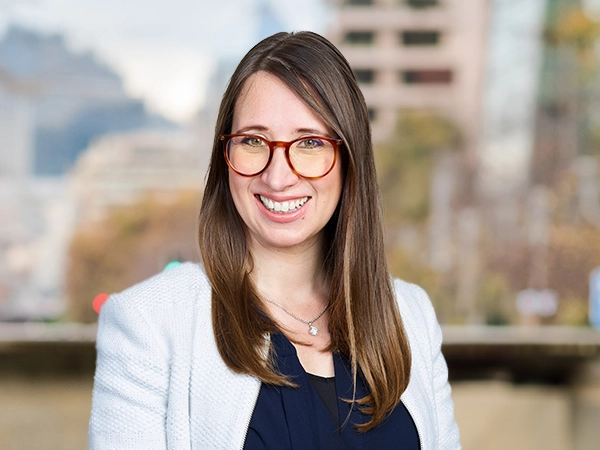Nathalie Duncan-Sletten outside in front of a blurred brown background featuring a building and mix of natural and urban elements.