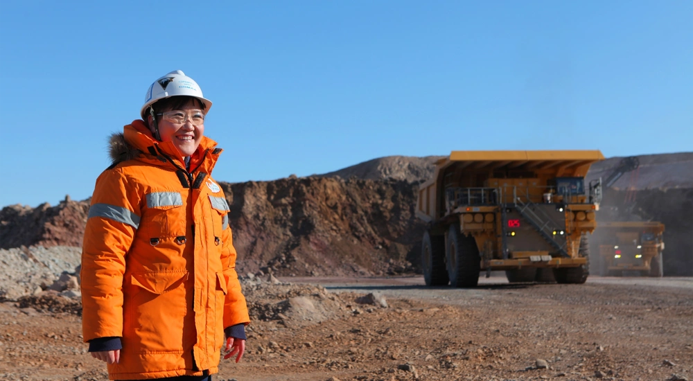 Woman standing in sandy construction site wearing orange hi vis and helmet