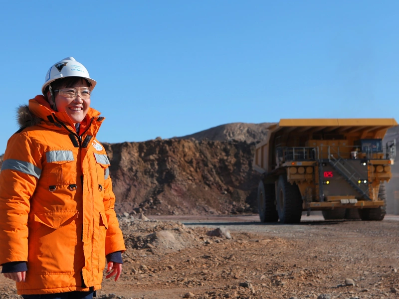 Woman standing in sandy construction site wearing orange hi vis and helmet