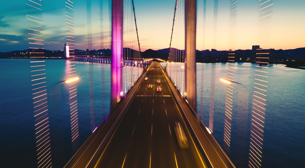 Road bridge over wide river at night with mountains in the background