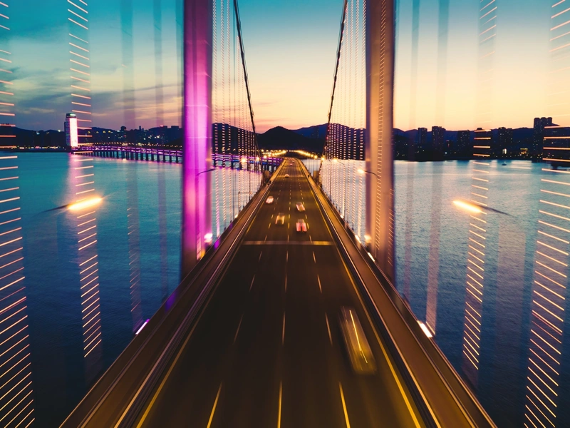 Road bridge over wide river at night with mountains in the background