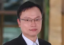 Tino Chang, Lead Director, outside in front of a blurred brown background featuring a building and mix of natural and urban elements.