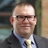 Portrait of Marc Fooks, UAE Infrastructure Lead, outside in front of a blurred brown background featuring a building and mix of natural and urban elements.