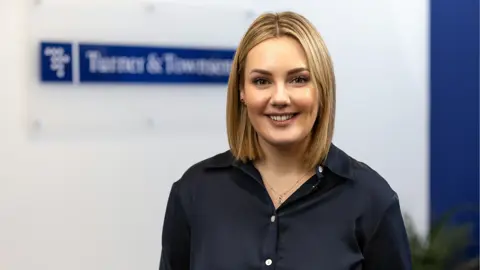 Portrait of Steph Marahall, Managing Director, UK Cost Management, standing in office in front of Turner & Townsend sign