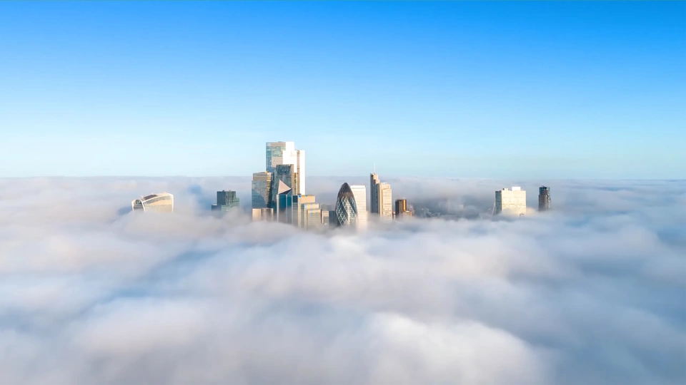 City skyline with modern skyscrappers rising above a layer of fog under a clear blue sky.
