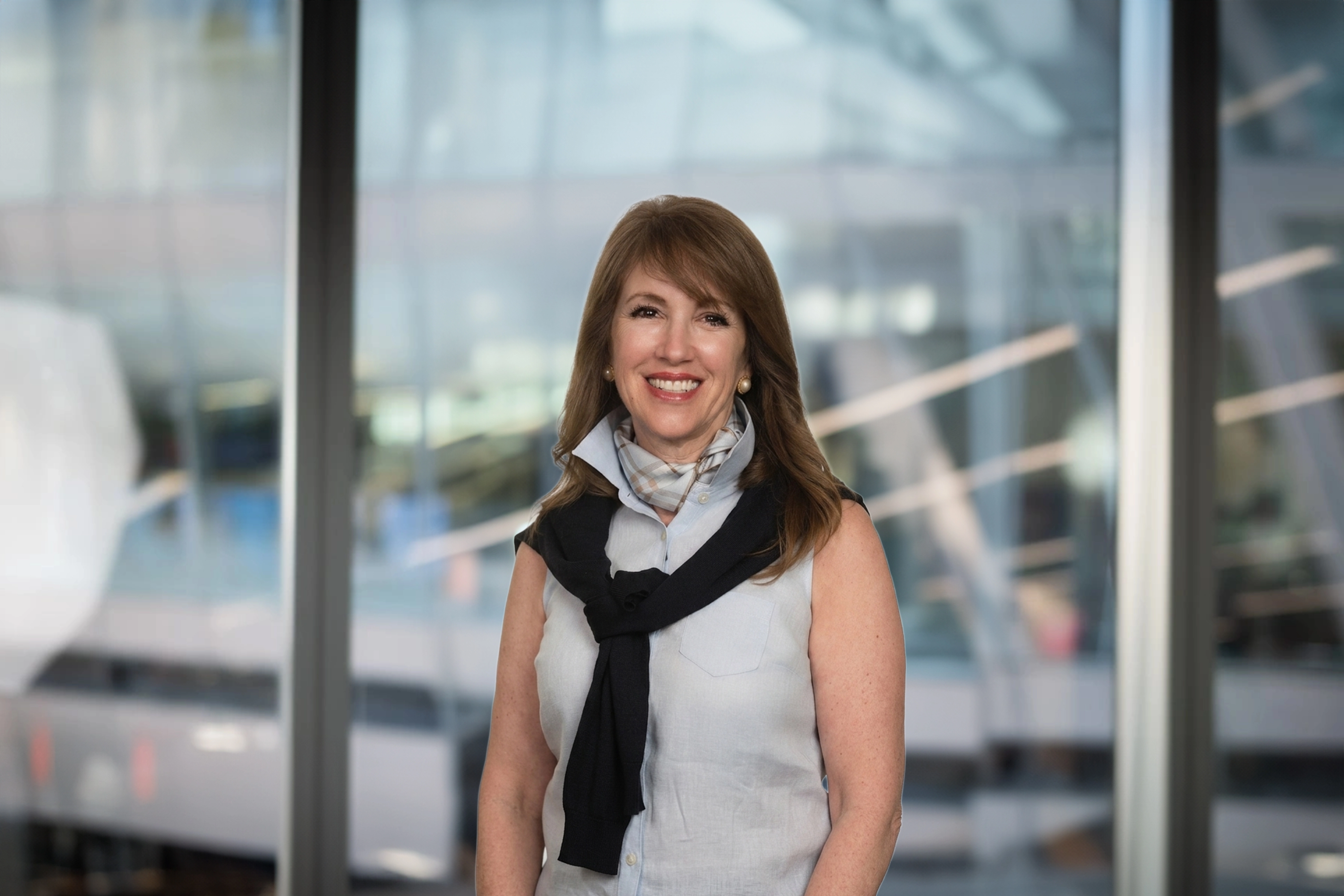 Christie Hartnett standing inside in front of a window displaying an outdoor urban setting, featuring modern architectural elements with clean lines. 