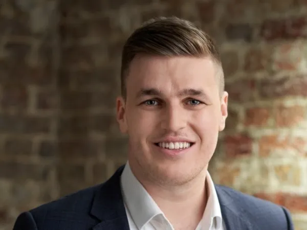 Portrait of Danny Waters, Associate Director, Standing against brown brick wall in blue suit