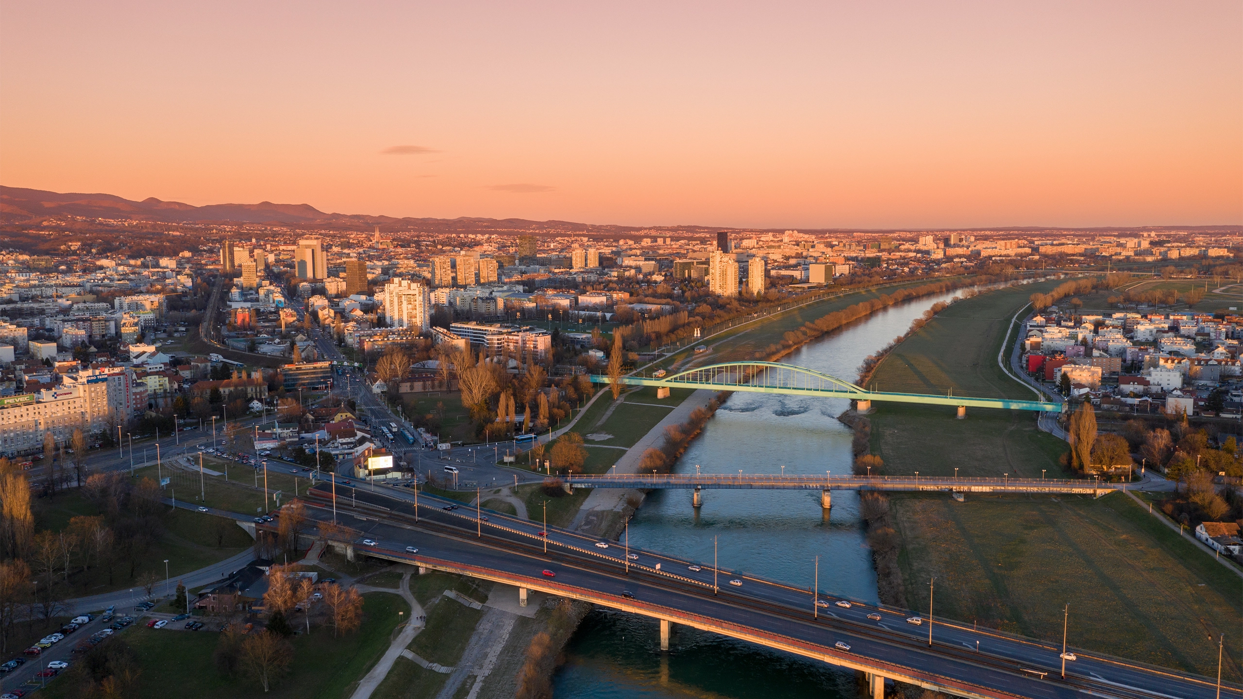 Aerial view of city at sunset with warm orange lisght, showing a river running through the centre.