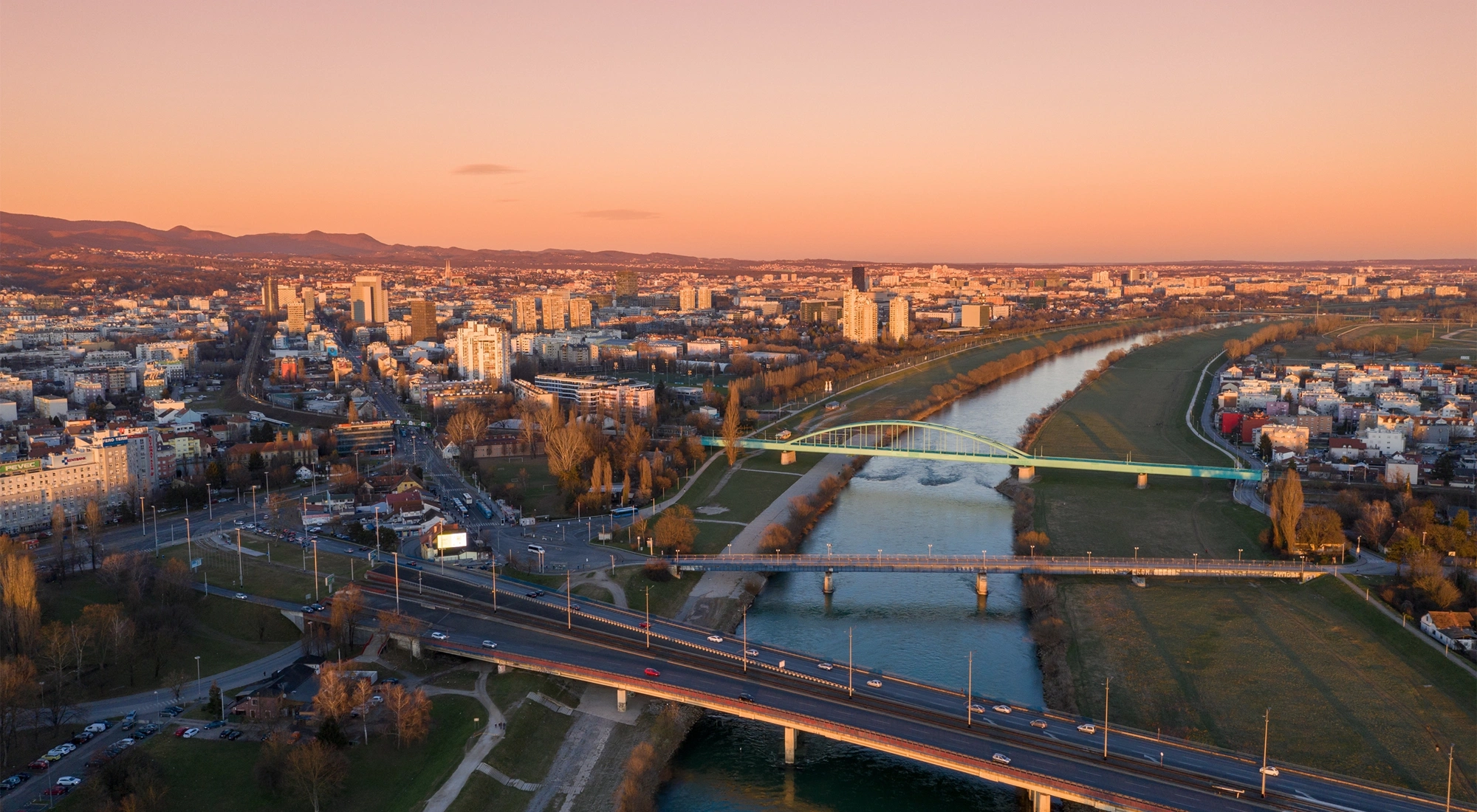 Aerial view of city at sunset with warm orange lisght, showing a river running through the centre.