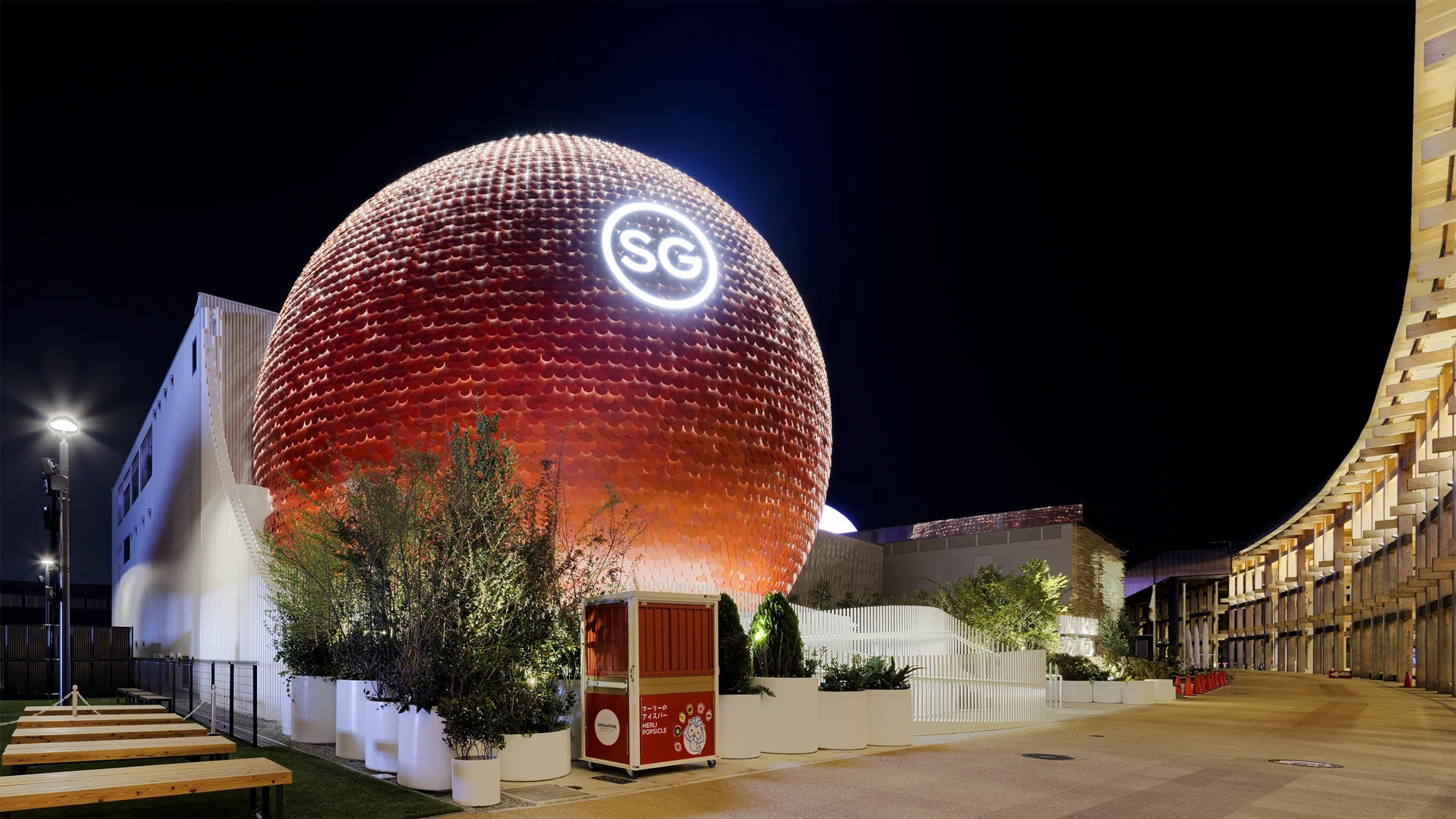 Night view of the Singapore Pavilion at Expo 2025 Osaka, Japan, featuring striking spherical red structure with the letters SG illuminated at the top.