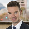 Portrait of Perry Knight, Vice President, standing outside featuring an urban cityscape with tall buildings and a mix of architectural styles. The scene includes some trees with autumn foliage, adding a touch of color.